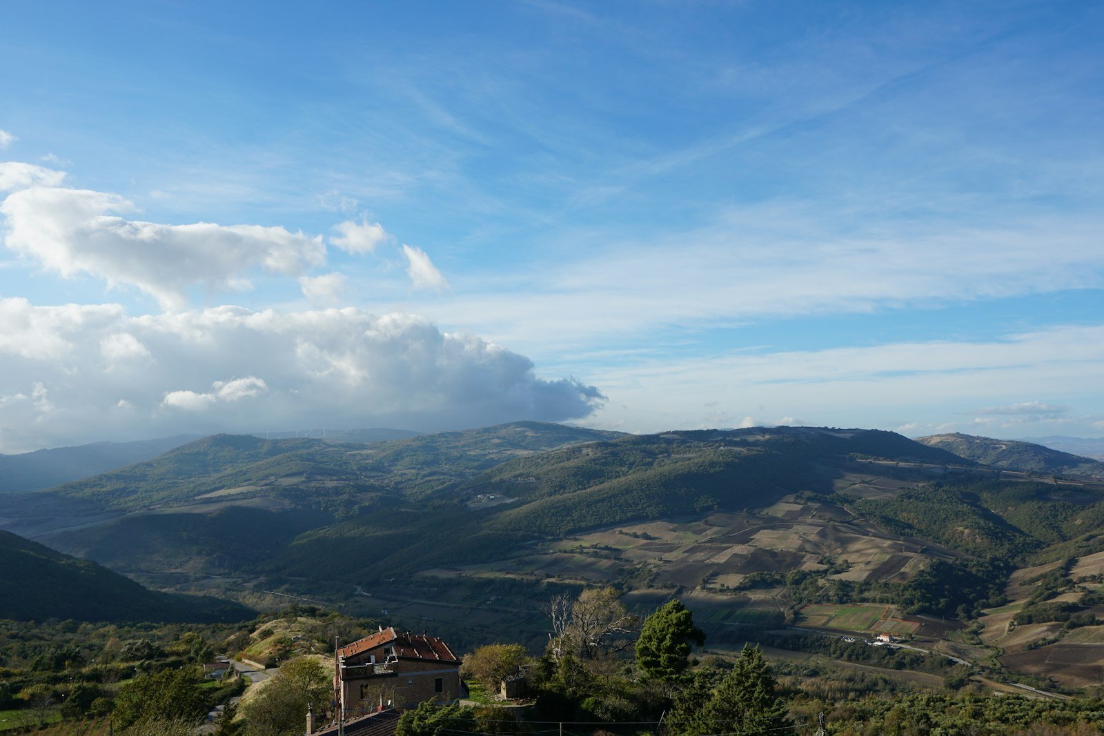 Vista panoramica della campagna pugliese da Bovino, con colline e una casa bianca in lontananza, sotto un cielo sereno.